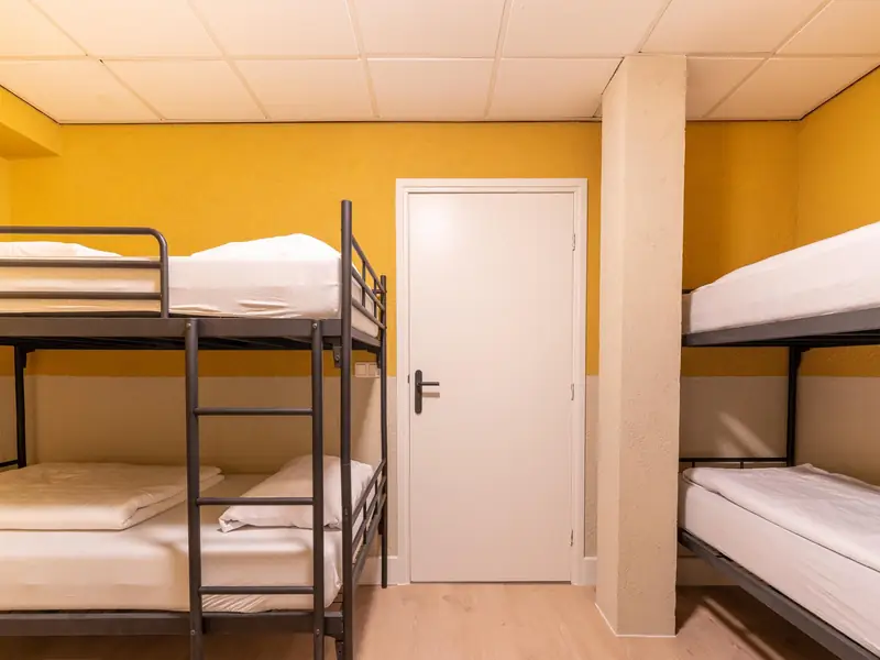 Slaapkamer met twee zwarte metalen stapelbedden en gele muren rond een witte deur.