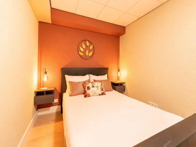 Slaapkamer met tweepersoonsbed, terracotta wand, gouden bladdecoratie en twee bedlampjes.