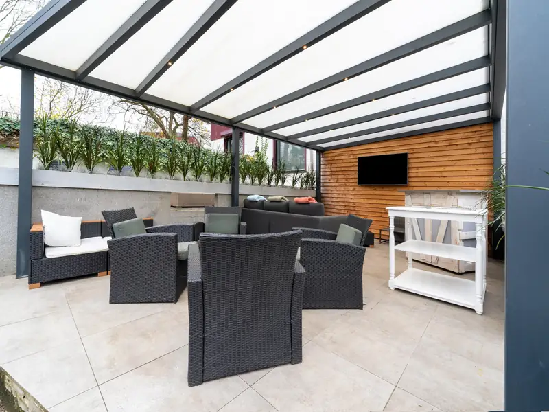Overdekte veranda met donkere wicker loungestoelen, een loungebank en een tv aan een houten wand.