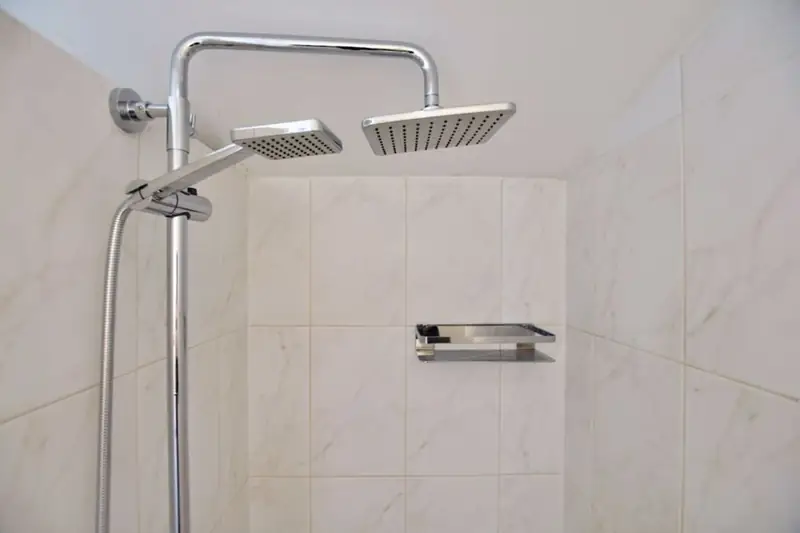 Verchroomde douchekolom met een vierkante regendouche, een handdouche en een wandrekje.