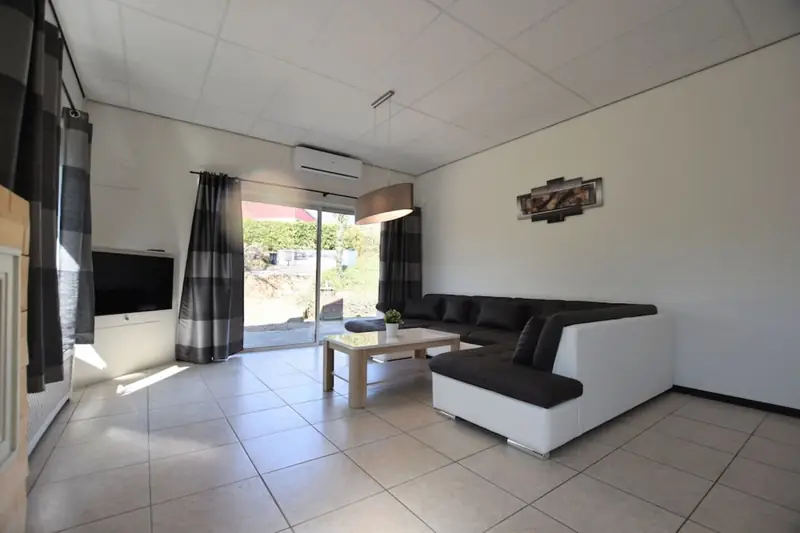 Woonkamer met grote hoekbank, salontafel, televisie en een schuifpui naar buiten.